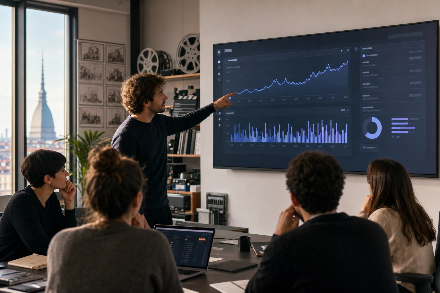 Un piccolo team di uno studio di produzione che esamina una dashboard di analisi di un canale YouTube su un grande schermo in un ufficio a Torino